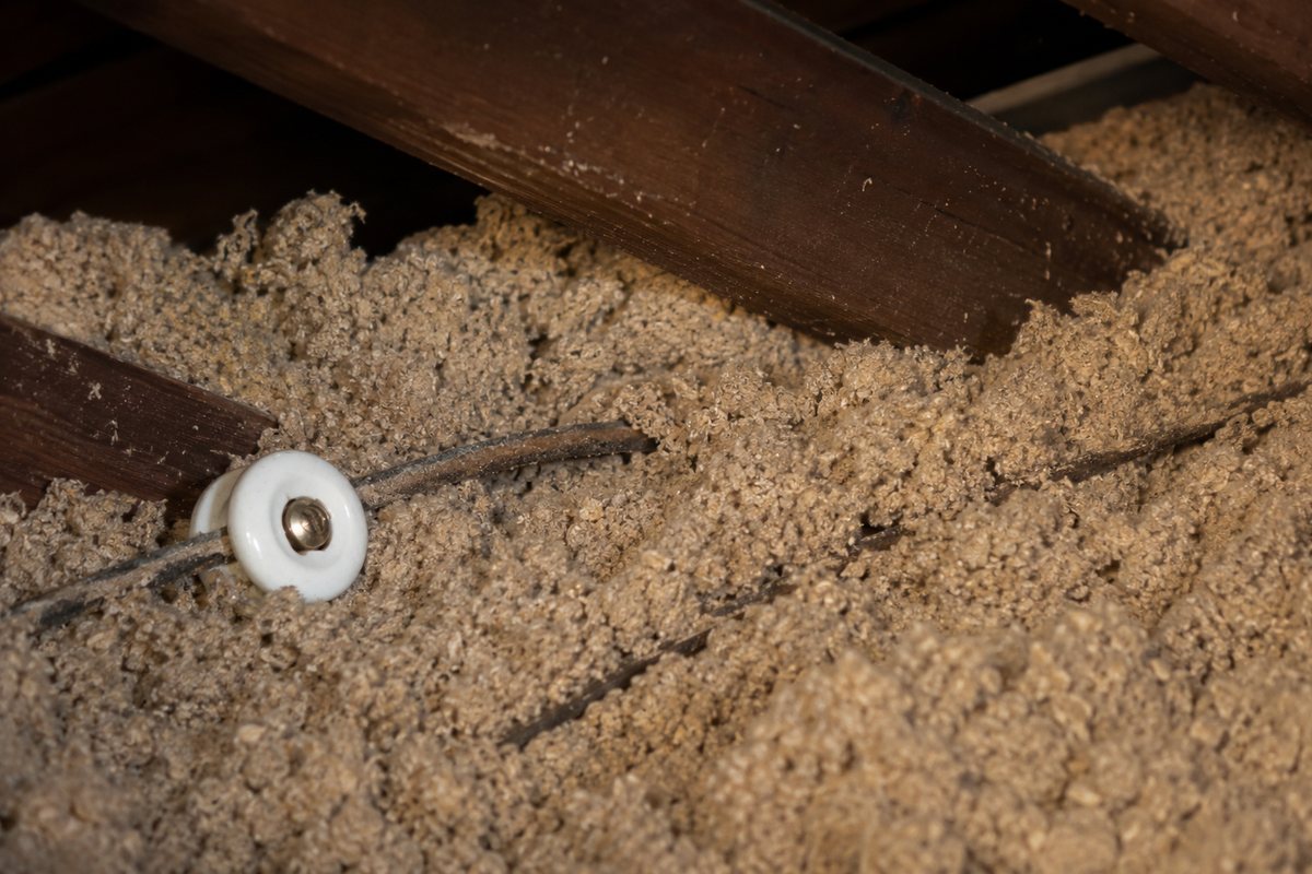 Old knob-and-tube wiring partly buried under blown-in attic insulation, which traps heat