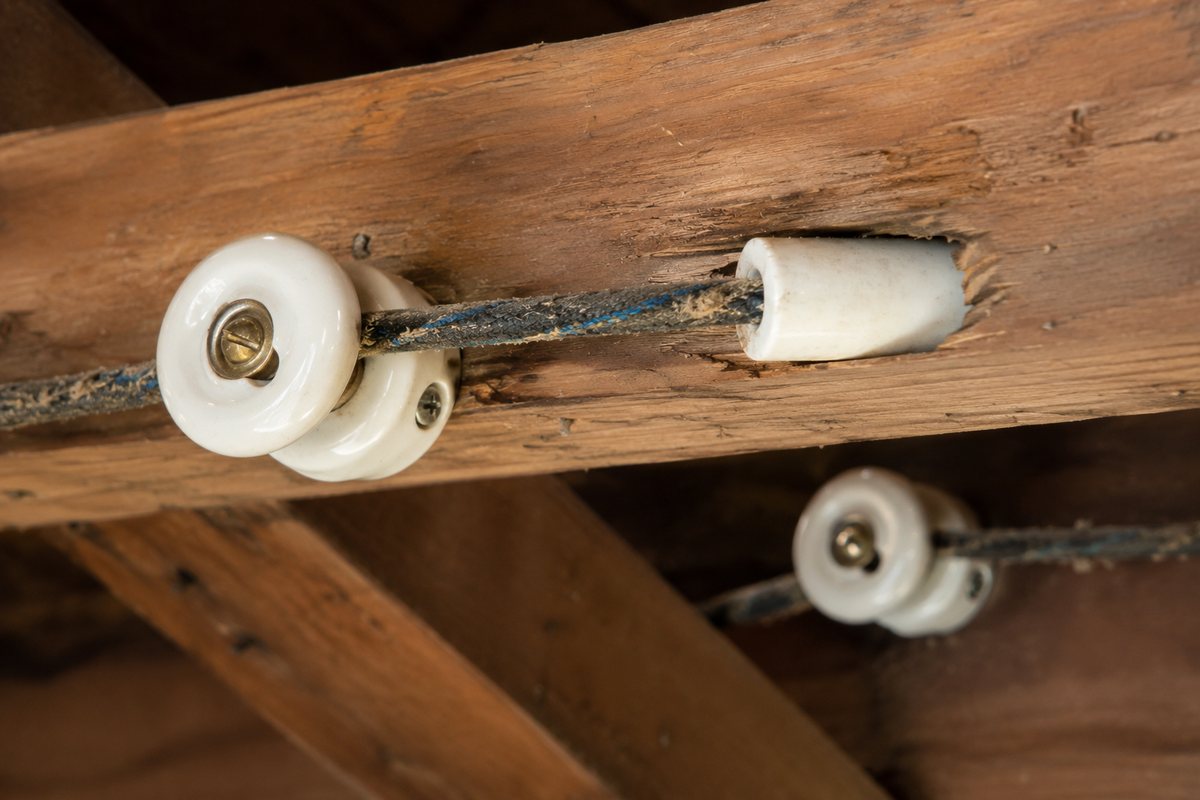 Close-up of original knob-and-tube wiring showing white ceramic knobs and a tube on a wooden joist
