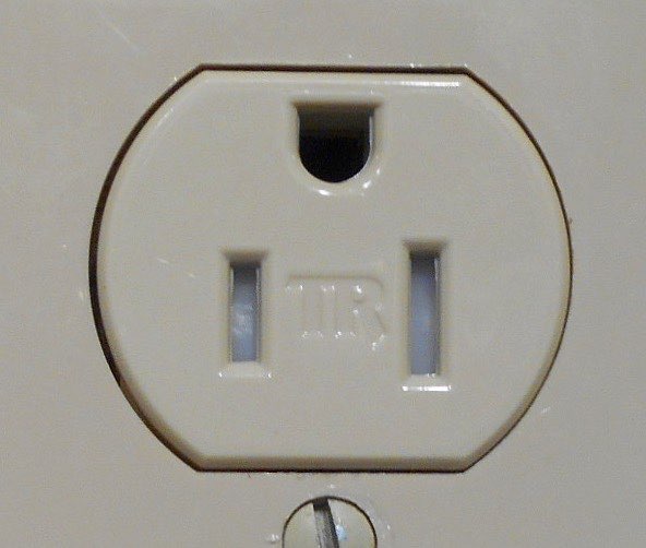 Close up of an ivory tamper resistant receptacle with pale shutters visible behind both vertical slots