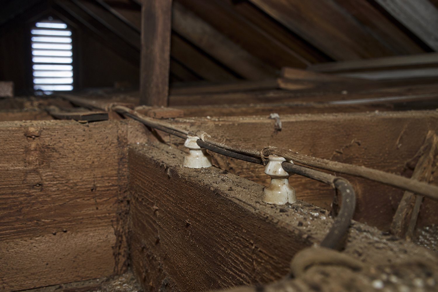Old knob-and-tube wiring with ceramic knobs running through attic joists